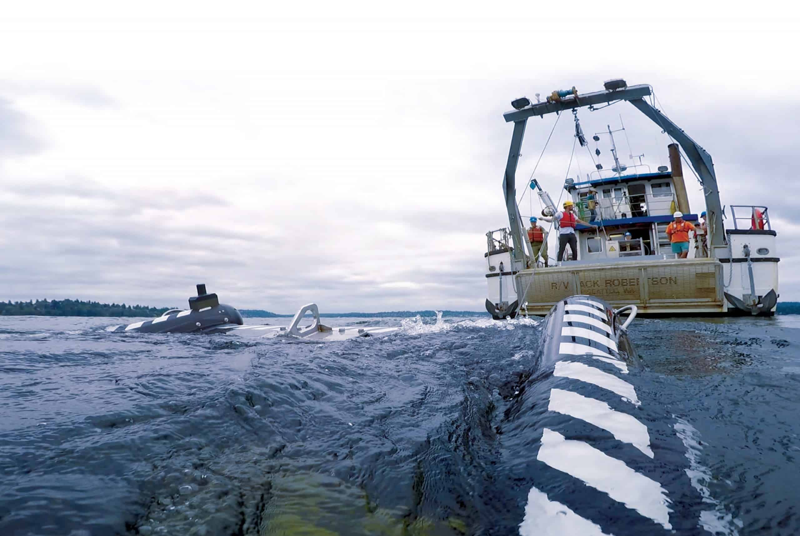 Shot taken with a camera mounted to the Multi-Sensor Towbody (MuST) instrument as it emerges from the depths of Lake Washington, the Research Vessel Jack Robertson is in the background with several researchers on deck.