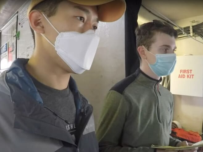 Two students, each wearing facemasks, aboard the research vessel.