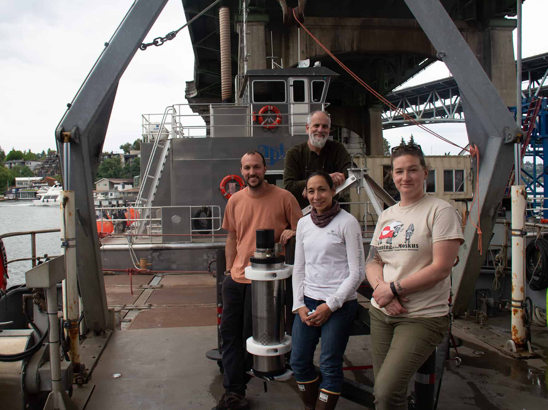 Four researchers stand on the deck of Research Vessel Jack Robertson, next to a scientific instrument that has just been tested in Lake Washington